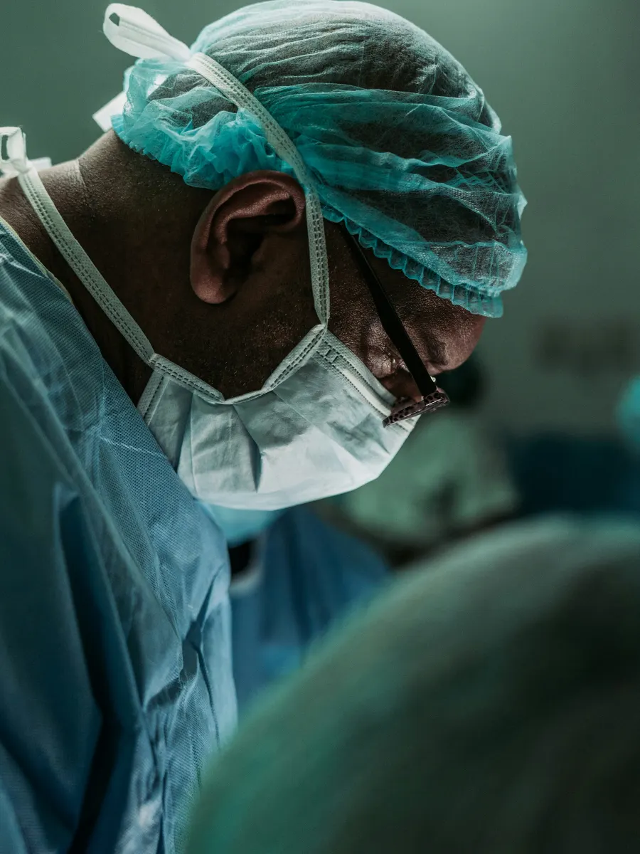 A clinician in scrubs and a surgical cap, concentrating